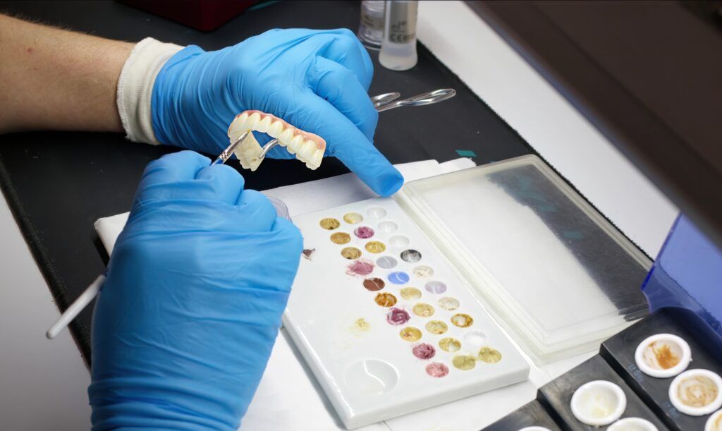 Dental technician in blue gloves holds a denture model while mixing tooth shade materials for a forensic DNA sample collection or court ordered DNA analysis concept.