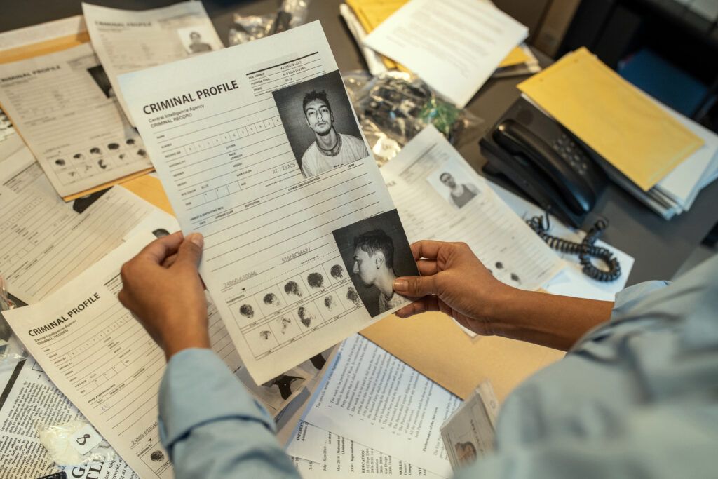Law enforcement officer reviewing a criminal profile document with fingerprints and photographs during a background investigation.