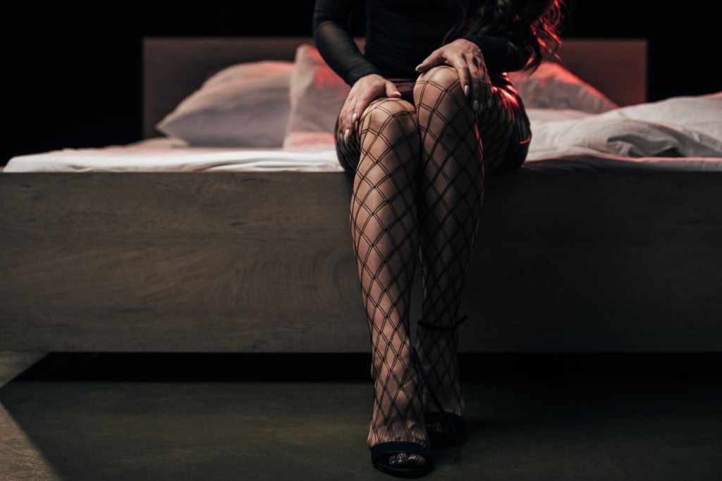 cropped view of prostitute in mesh stockings sitting on bed on black