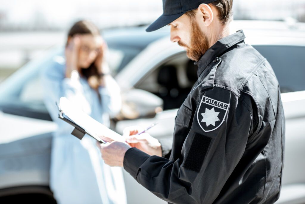 Police officer writing a roadside report with a stressed driver nearby, representing new impaired driving law enforcement in Canada