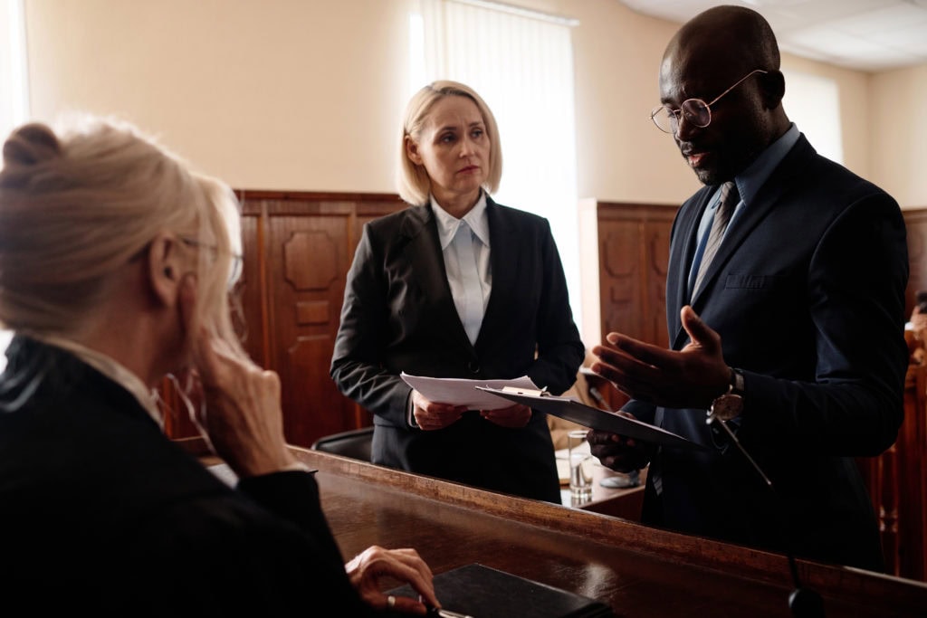 Defense and prosecution sides of court case standing in front of judge