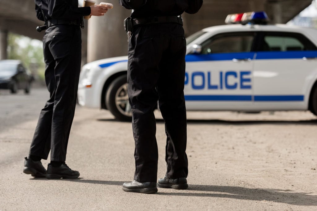 cropped shot of police officers standing in front of police car