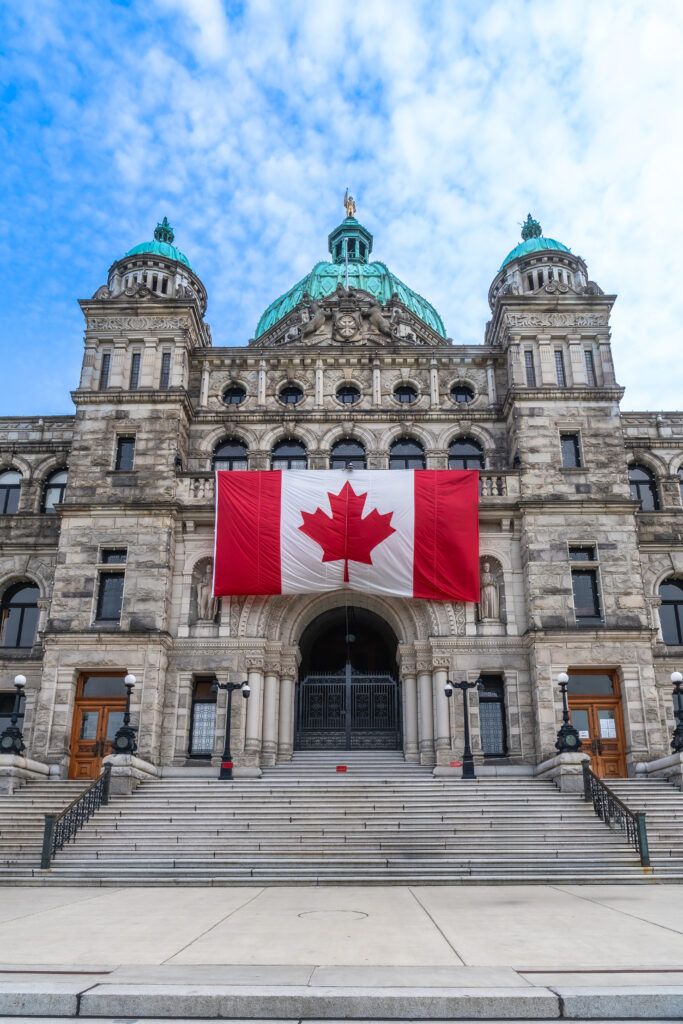 Canadian flag hanging in front of a historic government building, representing Canadian law and criminal justice for sexual assault charges in Canada.