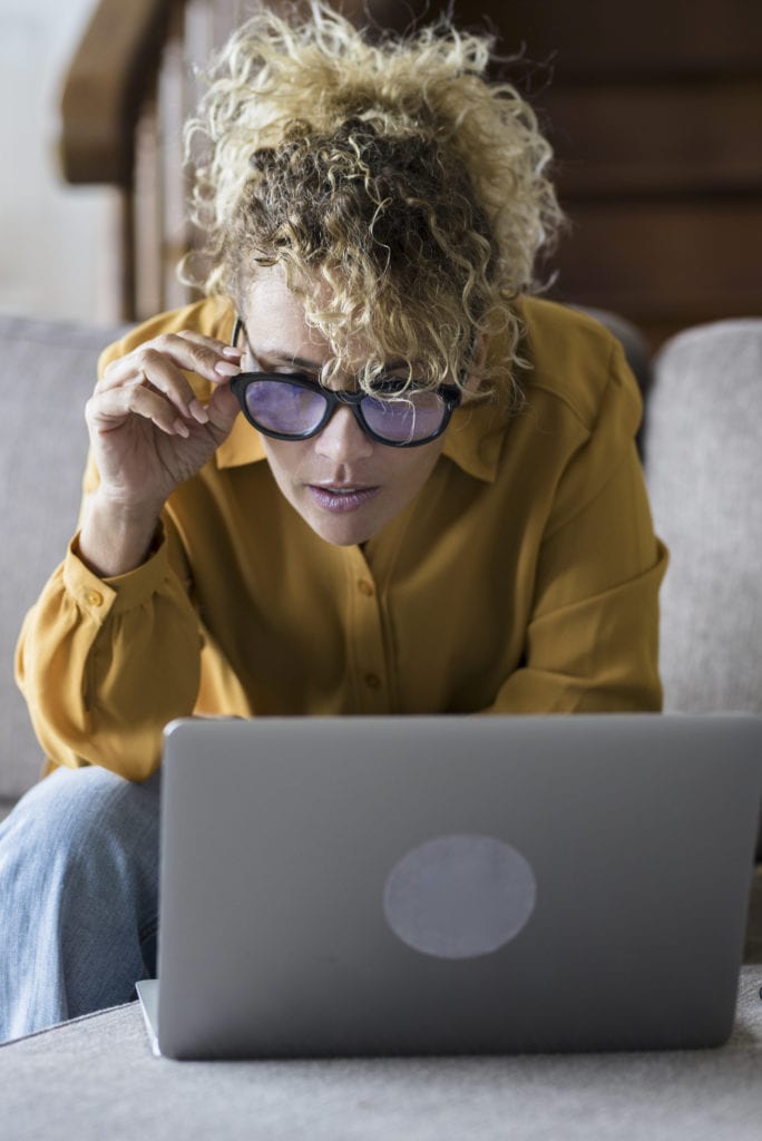 Beautiful cheerful blonde woman using silver laptop while sittin